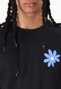 Sort bomulds t-shirt med en stor blå tusindfryd grafik med en hvid midte, rund halsudskæring og korte ærmer. Tekstureret, afslappet stof.