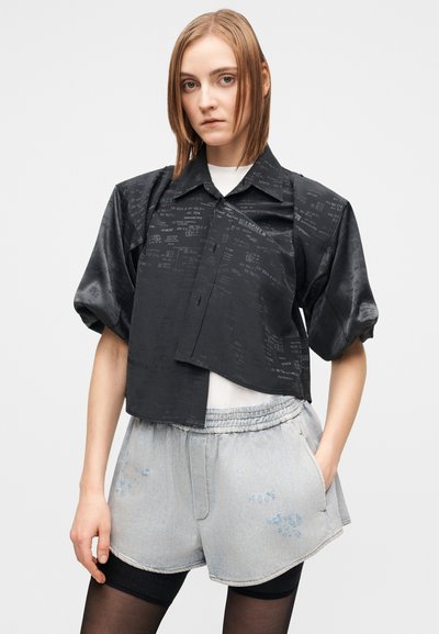 Μαύρο κοντομάνικο πουκάμισο με γυαλιστερό φινίρισμα και τυπωμένα μοτίβα κειμένου, συνδυασμένο με ανοιχτόχρωμα τζιν σορτς με ελαστική μέση και τσέπες.