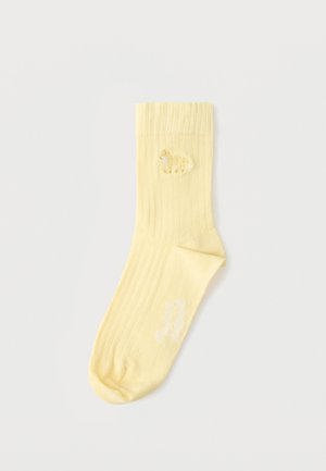 Világos sárga bordázott zokni kis hímzett sárga juhval a bokán és fehér szöveggel a talpon.