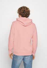 Sweat à capuche rose clair avec cordon de serrage, poche kangourou à l'avant, et poignets et ourlet côtelés. Texture de tissu douce, design simple.