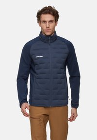 Marineblå isoleret jakke med quiltet front, glatte ærmer, høj krave og diskret hvidt logo. Lynlåslukning foran og sidelommer.