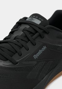 Juodas sportinis batas su tekstūruotu paviršiumi, turintis Reebok ženklą, tonuotomis raištelėmis ir guminiu pado akcentu.