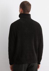 Black ribbed sweater with a high collar and long sleeves. Textured fabric with a relaxed fit, featuring side slits at the hem.