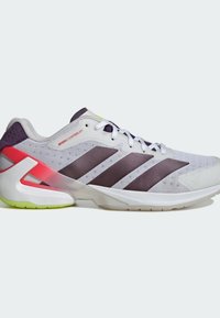 Baskets de course blanches et violettes avec trois rayures sombres, lacets blancs, support de talon rouge et semelle vert clair sous le talon.