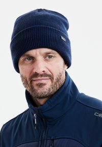 Merihenkinen neulepipo, jossa on ribbiä muistuttava rakenne ja pieni logopatchi. Yhdistetty samansävyiseen siniseen takkiin.