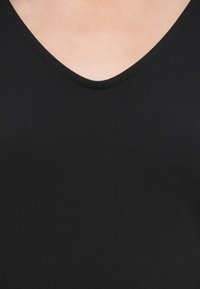 Top negru fără mâneci cu un design în formă de V. Fabricat dintr-un material neted, elastic, cu un finisaj curat și fără modele sau embellismente vizibile.