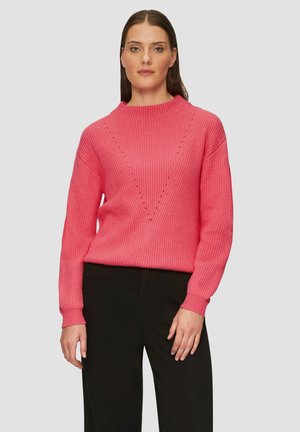 Sweater côtelé rose vif avec un col haut, présentant un motif en V et des accents en forme de diamant. Assorti à un pantalon noir pour le contraste.