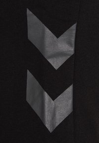 Dos formas de chevron plateadas y reflectantes apuntando hacia abajo sobre un fondo de tela negra texturizada.