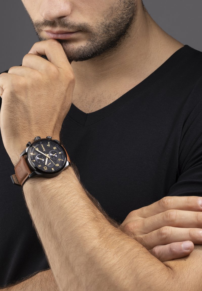 Montre chronographe avec un cadran noir, des accents dorés et un bracelet en cuir marron. Présente trois sous-cadrans et des index des heures contrastés.