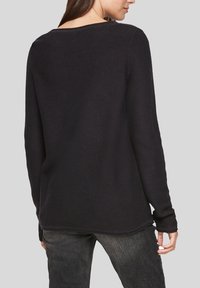 Pull long à manches longues noir en tricot avec une coupe décontractée, un col arrondi et un tissu texturé. Se termine juste en dessous de la taille, avec des fentes sur les côtés.