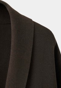 Tissu tricoté marron foncé montrant un gros plan du col plié et de la zone de l'épaule d'un vêtement.