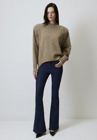 Maglione beige lavorato a maglia con collo alto, polsini e orli a coste, abbinato a jeans a svasare blu scuro e tacchi a punta neri.