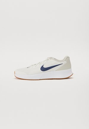 Chaussure de course blanche avec logo Nike swoosh bleu marine et semelle couleur gomme, vue de profil sur un fond uni.