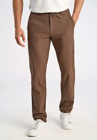 Brązowe spodnie z lnu z relaksowanym krojem, elastycznym pasem i zwężanymi nogawkami, zestawione z białymi trampkami. Prosty design, bez widocznych wzorów.
