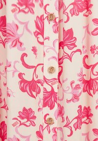 Stof met bloemenpatroon in roze en koraalkleuren; heeft een houten knop met "BIZUU" merknaam op een romige achtergrond.