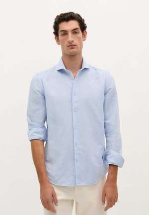 Camisa abotonada de color azul claro hecha de una tela suave. Presenta un cuello clásico, mangas largas arremangadas en los puños y detalles de costura sutiles.