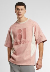 Light pink oversized t-shirt with a textured finish, featuring a large "81 another" graphic and cream-colored side panels. Short sleeves.