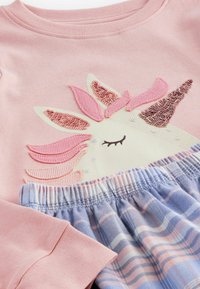 Lyserød bomuldsbluse med et enhornedesign med palietter; blå og lyserøde ternede shorts med elastisk talje.