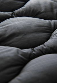 Tessuto nero trapuntato che mostra una texture morbida e imbottita con un sottile motivo a griglia, che mette in risalto forme arrotondate e contrasti di luce e ombra.