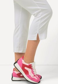 Baskets de sport avec des panneaux en daim rose et rouge, des accents blancs et des semelles en caoutchouc noir. Pantalons blancs fuselés avec un détail fendu à l'ourlet.