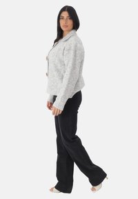 Szary płaszcz z wełny z szerokim kołnierzem, trzema dużymi guzikami i prążkowanymi mankietami, w połączeniu z czarnymi spodniami w stylu dzwonów i sandałami na odsłonięte palce.