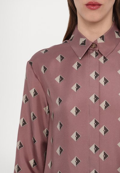 Silkbluse i en mauve farge med et geometrisk mønster av kremfargede og svarte diamantformer, med spiss krage og knappeåpning.