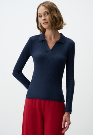 Marineblauwe geribbelde poloshirt met lange mouwen en een v-hals, gecombineerd met losse rode broeken.