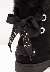 Černé semišové kotníkové boty s huňatým svrškem, dekorační stuhou se flitry, pevnou podrážkou a kovovými očky na šněrování.