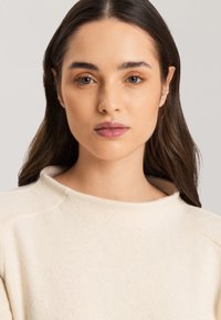Cremiger Pullover mit hohem Kragen, weichem Material und dezenten Stichdetails. Entworfen für eine lockere Passform.