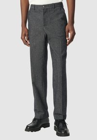 Pantaloni in misto lana grigio scuro con taglio dritto, passanti per la cintura, tasche anteriori e chiusura a bottone. Indossati con scarpe nere stringate.