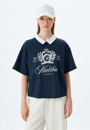 T-paita lyhyillä hihoilla, jossa on valkoinen kaulus ja graafinen printti, jossa lukee "Malibu, Los Angeles". Kevyt materiaali, rento leikkaus, näkyvät ompeluyksityiskohdat.