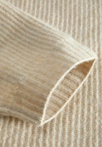 Manga acanalada de suéter de punto en lana beige claro, con una textura suave y un borde ligeramente enrollado, mostrando detalles de hilo finos.