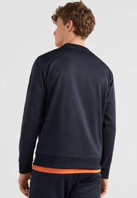 Marineblauwe sweatshirt met een gladde textuur, geribbelde manchetten en een gebandezoom; heeft een oranje accent eronder voor contrast.