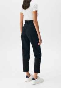 Jean noir taille haute avec une légère coupe fuselée, doté d'une ceinture extensible et de deux poches arrière, porté avec des baskets blanches.