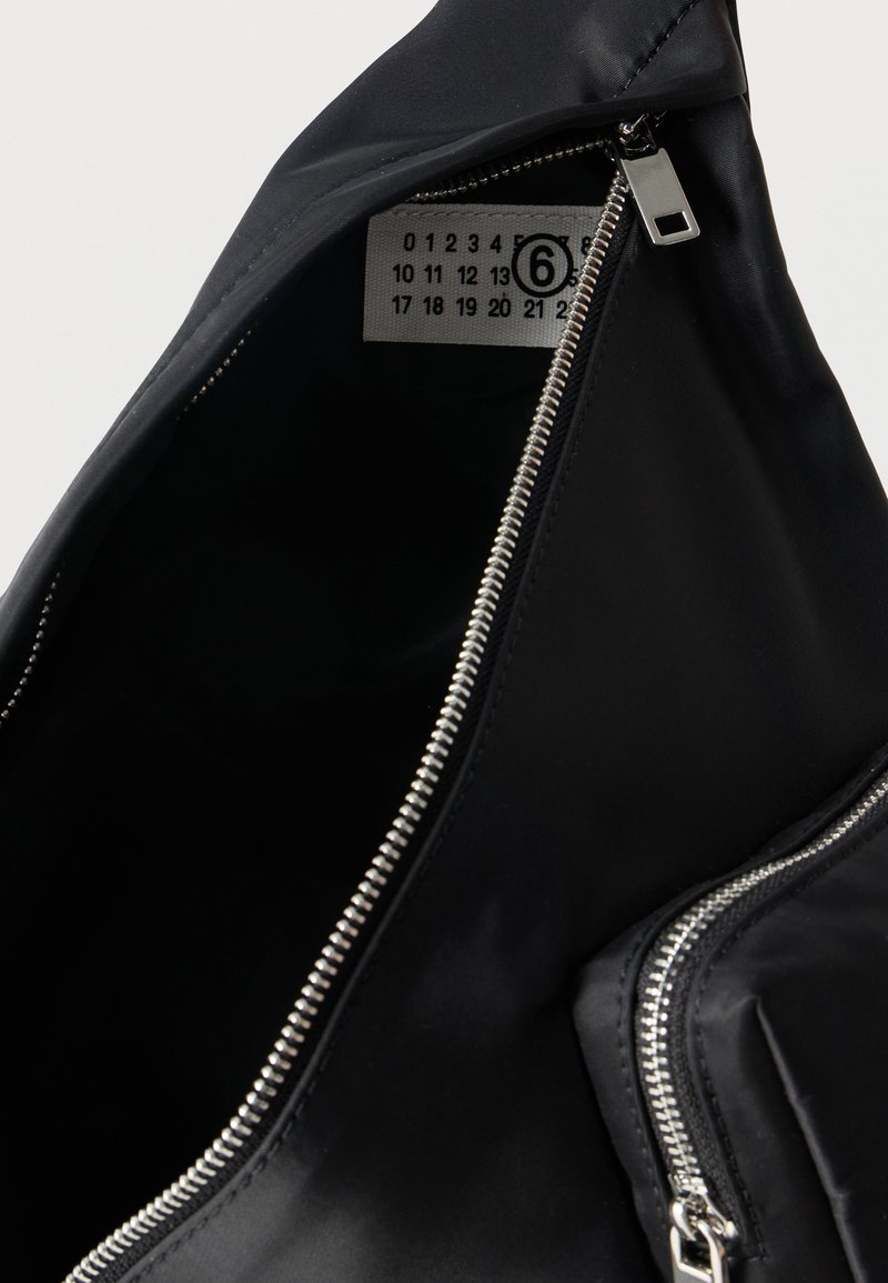 Sac noir partiellement ouvert avec une fermeture éclair argentée et une étiquette à l'intérieur montrant un numéro 6 cerclé parmi d'autres chiffres sur un tissu blanc.