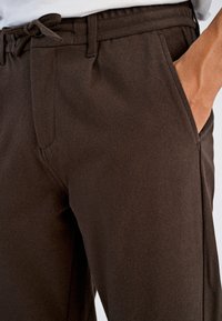 Brązowe spodnie dresowe z fakturowanego materiału, z elastyczną talią i sznurkiem oraz bocznymi kieszeniami na przechowywanie.