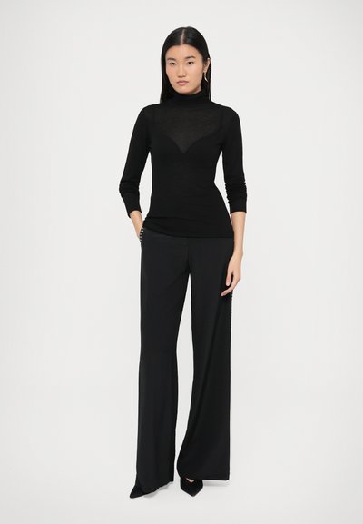 Czarny golf z przezroczystym panelem, zestawiony z czarnymi szerokimi spodniami z wysokim stanem. Oba elementy mają gładką teksturę i elegancki design.