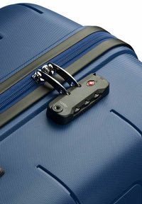 Valigia rigida blu navy con finitura testurizzata, dotata di zip nere, doppie zip e una serratura approvata dalla TSA fissata sul lato.