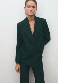 Tamnozeleni krojeni dupli sako s uskim reverima i dva prednja đepa. Glatka tkanina s čvrstim krojem i kontrastnim gumbima.