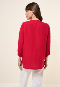 Blusa rossa a maniche lunghe con vestibilità comoda, caratterizzata da scollatura rotonda e sottili dettagli con bottoni sulle maniche. Tessuto leggero.