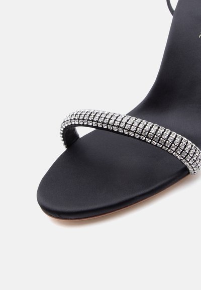 Μαύρο σανδάλι με ανοιχτά δάχτυλα και ένα μόνο λουρί διακοσμημένο με πολλαπλές σειρές λαμπερών κρυστάλλων.