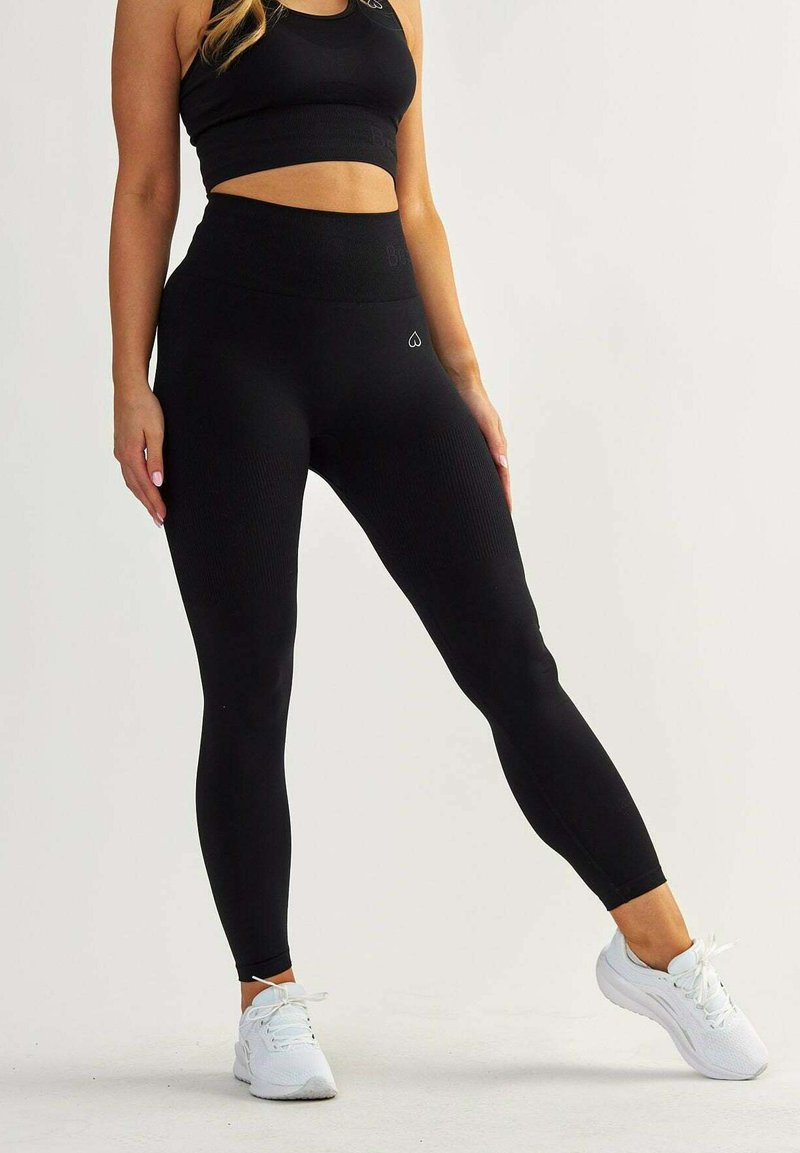 Black high-waisted leggings made of ribbed fabric, featuring a seamless design. Paired with white athletic shoes.