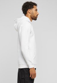 Sweatshirt à capuche blanc avec une poche kangourou, manches longues et poignets côtelés. Tissu doux avec une texture lisse.