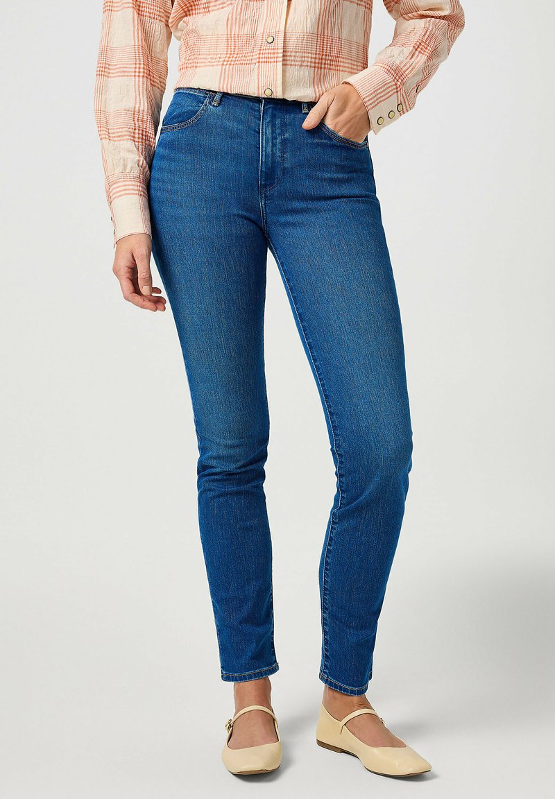 Jeans skinny in tessuto denim con una texture liscia, caratterizzati da una vita media e un design a cinque tasche standard. Abbinati a ballerine di colore chiaro.