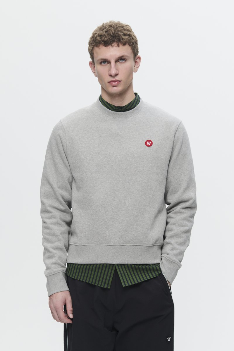 Gray sweatshirt with a round neckline and ribbed cuffs, featuring a red logo on the left chest. Underneath, a green striped collared shirt is visible.