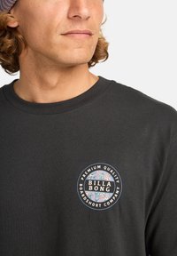 Mustmust särk musta puuvillast, millel on ümmargune graafiline logo lillemotiividega. Ümmargune kaelus ja lühikesed varrukad. Sile tekstuur.