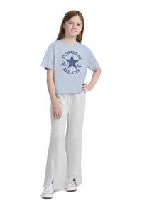 Šviesiai mėlynas sutrumpintas t-shirt'as su jūrinės spalvos "CONVERSE ALL STAR" spauda, derinamas su pilkomis plačiomis sportinėmis kelnėmis su šoninėmis plyšimis ir baltais sportbačiais.