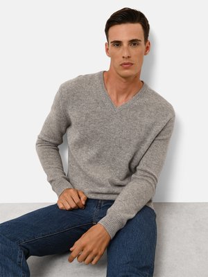 Szary sweter w serek wykonany z dzianiny, posiadający długie rękawy i ściągacze przy mankietach, zestawiony z niebieskimi dżinsami. Prosty i elegancki design.