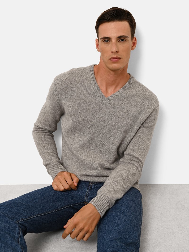 Grau v-Ausschnitt Pullover aus Strickmaterial, mit langen Ärmeln und gerippten Bündchen, kombiniert mit blauen Jeans. Einfaches und klares Design.