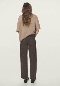 Przewymiarowany beżowy sweter z dzianiny w zestawieniu z wysokim stanem ciemnobrązowych spodni o szerokich nogawkach, charakteryzujących się luźnym krojem i minimalistycznym wykończeniem.